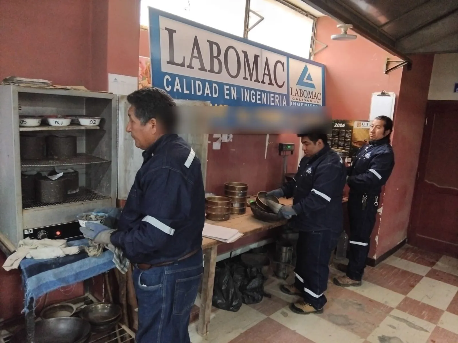 Técnicos en el laboratorio: uno retira muestras del horno de secado y otros dos trabajan con tamices.